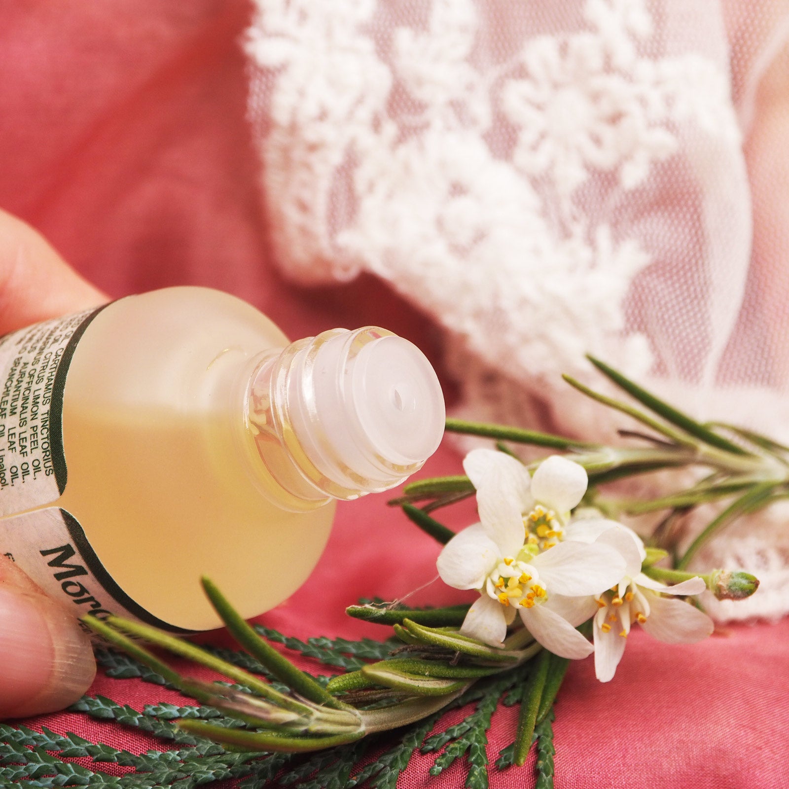 Morgenrot Körperöl in geöffneter 15ml Glasflasche mit TRopfeinsatz. Im Hintergrund weiße Tischdecke mit Spitze und einzelnem Tannenzweig